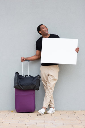 Smiling man in casual attire leaning against a wall, laughing while holding a blank white signの写真素材
