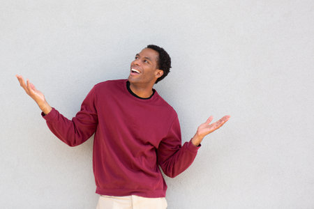 A man wearing a red sweater stands with his arms open and smiling, facing to the side against a grey wallの写真素材