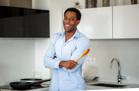 Smiling man standing confidently in a modern kitchen, holding a wooden spoon while preparing to cookの写真素材