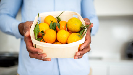 A close-up shot of a person holding a basket filled with fresh tangerines, some with leaves still attachedの写真素材