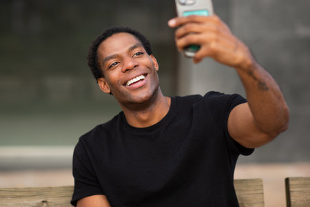 A man in a black t-shirt taking a selfie with a smartphone while smiling