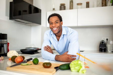 A man in a blue shirt stands in a modern kitchen, smiling at the cameraの写真素材