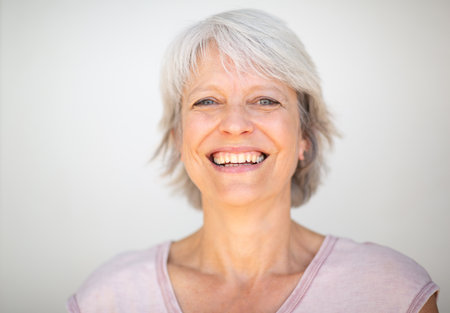 Bright portrait of a joyful senior woman with short grey hair and a big smile, wearing a light pink shirt, against a plain white backgroundの写真素材