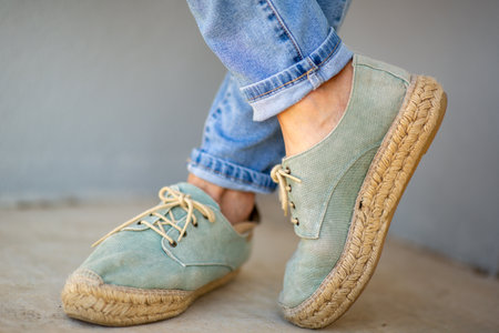 Detailed view of light green espadrille-style shoes with woven jute soles, paired with blue jeans rolled at the ankleの写真素材