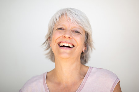 Portrait of a smiling woman with short gray hair wearing a light pink shirt, looking directly at the camera on a plain white backgroundの写真素材