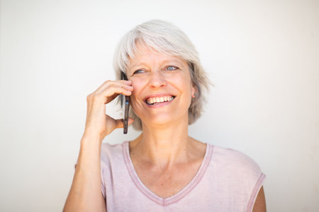 Close-up portrait of a mature woman with short gray hair, smiling as she talks on a mobile phoneの写真素材