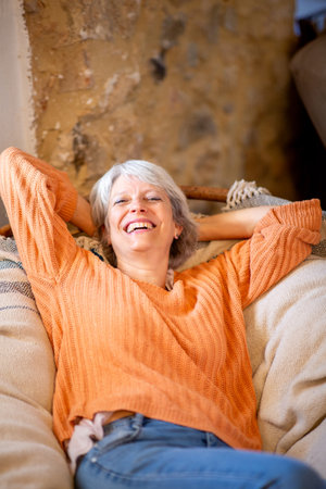 A happy senior woman with grey hair is seen reclining comfortably on a couch, smiling and laughingの写真素材