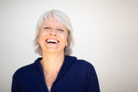 Portrait of a cheerful mature woman with short gray hair, wearing a navy blue jacket and smiling widely while looking at the cameraの写真素材