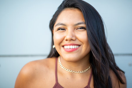 Close-up portrait of a smiling woman with long dark hair, wearing a gold chain necklace and brown topの写真素材