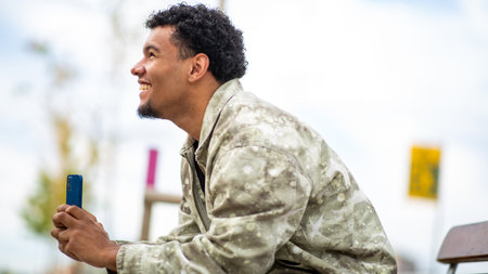 Young man outdoors, smiling and looking up while holding his smartphone, enjoying a relaxed momentの写真素材