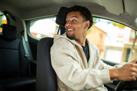 Young man in a beige hoodie smiling and looking back over his shoulder while driving a carの写真素材
