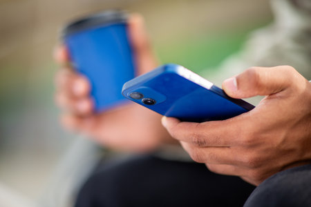 Close-up of a person holding a blue smartphone and a blue coffee cup. The focus is on the hands and the mobile deviceの写真素材