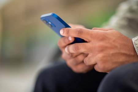 Close-up of a person's hands holding a blue smartphone, captured in an outdoor setting with a blurred backgroundの写真素材