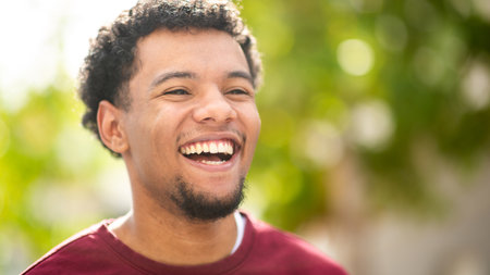 Young man with curly hair and a big smile enjoying a bright day outdoors with a green, blurred backgroundの写真素材