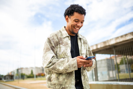 Young man smiling as he looks down at his smartphone while outdoors on a sunny dayの写真素材