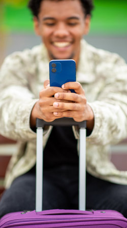 Close-up view of a smiling man using his smartphone while resting his hands on a purple suitcase handleの写真素材