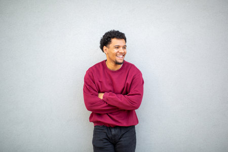 Young man wearing a red sweater and smiling with arms crossed while standing against a gray wallの写真素材