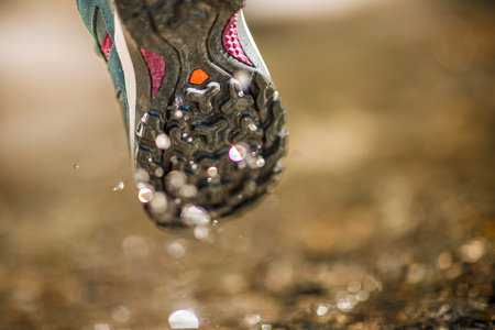 Close-up view of the bottom of a hiking shoe, highlighting the tread and water droplets as the shoe lifts off the groundの写真素材