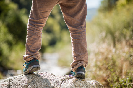 Close-up view of a person standing on a rock outdoors, with hiking shoes and beige pants visibleの写真素材