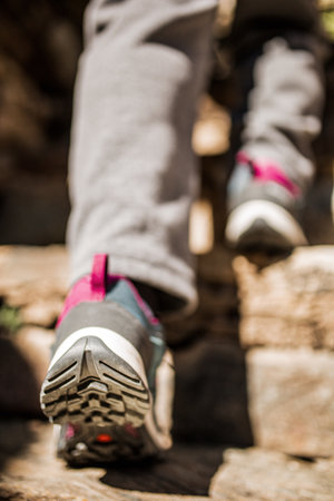 A back view of a person wearing gray and pink hiking shoes while climbing rugged stone stepsの写真素材