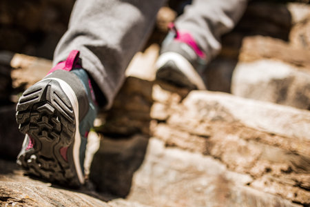 A close-up view of a person wearing gray and pink hiking shoes while ascending rocky stepsの写真素材