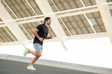 A man dressed in athletic wear running on a paved road under a modern structure during an outdoor...