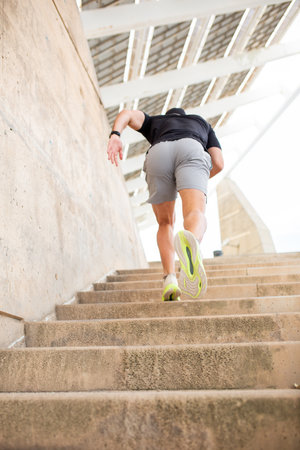 A rear view of a man in a black t-shirt, gray shorts, and white sneakers with green soles running...