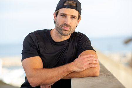 Close-up portrait of a man in sportswear leaning on a concrete wall, looking at the camera with a...