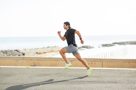 Athletic man with athletic wear running on a flat road near the sea with rocky coastal scenery visible in the background on a bright dayの写真素材