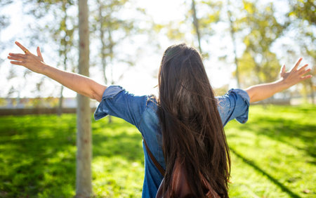 A woman in a denim outfit stands with her back to the camera, arms open wide as she embraces the...