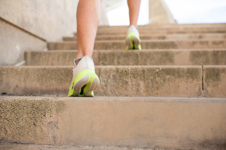 A close-up view of a person's legs in white sneakers with yellow soles running upstairs on concrete...