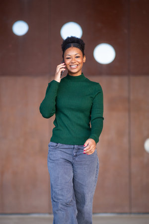 Portrait of a young woman with natural hairstyle wearing a green ribbed sweater and jeans, smiling...