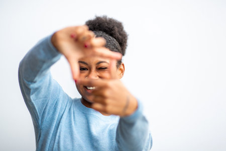 Smiling woman in a blue sweater creating a frame gesture with her hands against a clean white...