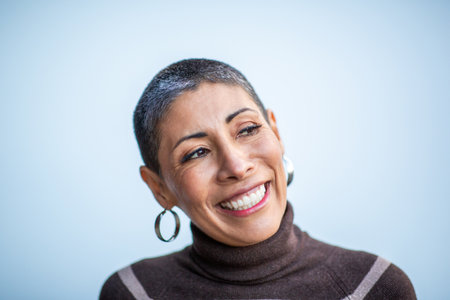 A close-up of a smiling woman with short hair and hoop earrings, wearing a brown striped sweater and...