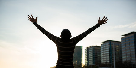 A woman in a striped sweater stretches her arms upward while facing the city skyline, capturing a...