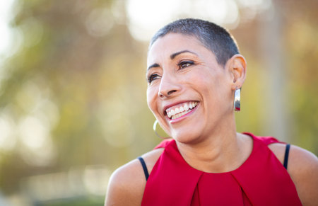 Close-up portrait of a woman in a red sleeveless top smiling brightly with a blurred outdoor backgroundの写真素材