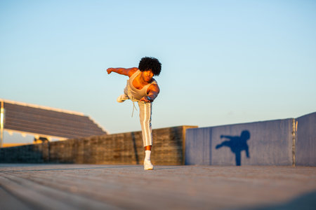 Muscular young man frozen mid-pose in a dynamic one-legged balance position outdoors. Early morning golden light enhances this intense moment of control and strengthの写真素材
