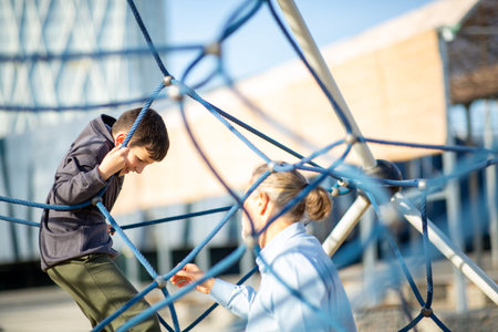 Young boy climbs on a net structure at a modern playground while his grandfather reaches out to assist him on a sunny dayの写真素材