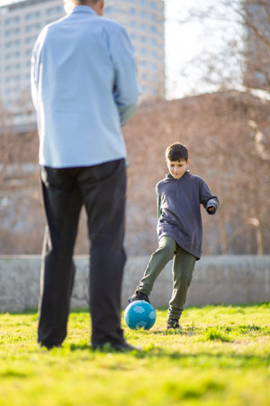 A concentrated young boy prepares to kick a blue soccer ball while playing with his grandfather on a bright grassy fieldの写真素材