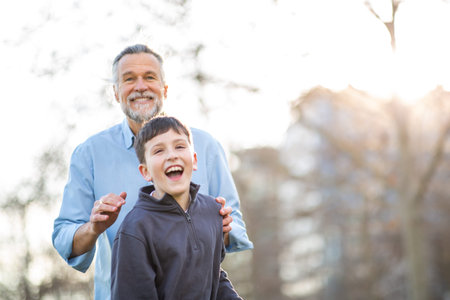 A joyful father places his hands on his laughing sonâs shoulders while they enjoy a happy moment together in a bright outdoor parkの写真素材