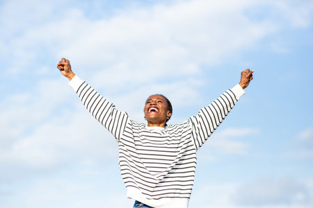 Young woman expressing joy and energy with a wide smile and arms raised triumphantly in the open air on a sunny day