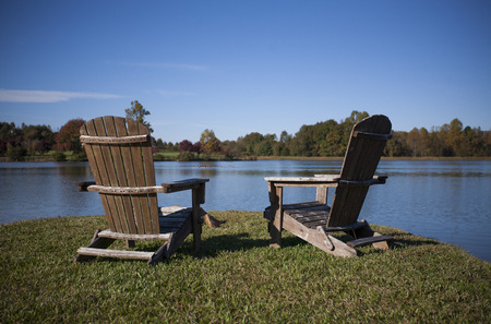Pair of Adirondack Chairs Sitting Next to a Lake in Autumnの写真素材