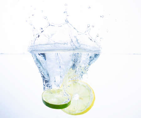Slice of Lemon and Lime Splashing into Water with a White Backgroundの写真素材