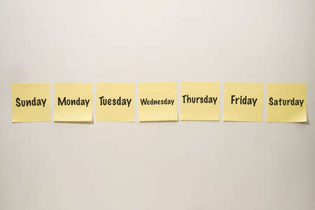 Yellow Sticky Notes Lined up on a White Background with the Days of the Week Written on themの写真素材