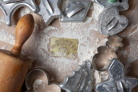 Merry Christmas Tin Stencil in Flour Surrounded by Holiday Cookie Cuttersの写真素材