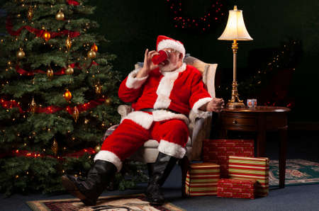 Santa Claus Relaxing in a Chair and Drinking from a Red Cupの写真素材