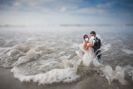 Bride and Groom Wedding Cake Topper with Surgical Masks Being Hit with a Wave in the Oceanの写真素材