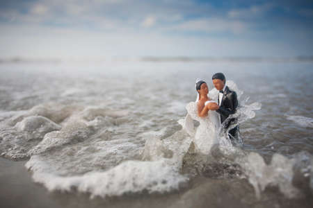 Bride and Groom Wedding Cake Topper Being Hit with a Wave in the Oceanの写真素材