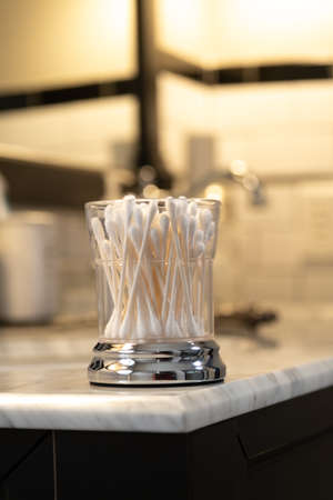 White Cotton Swabs in a Glass Container on the Edge of a Bathroom Vanityの写真素材