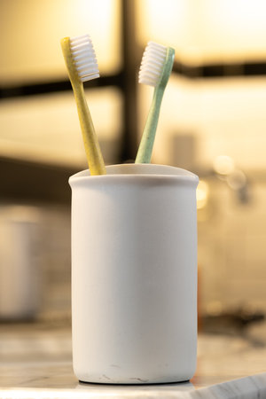 Toothbrushes in a White Cup on the Edge of a Bathroom Vanityの写真素材